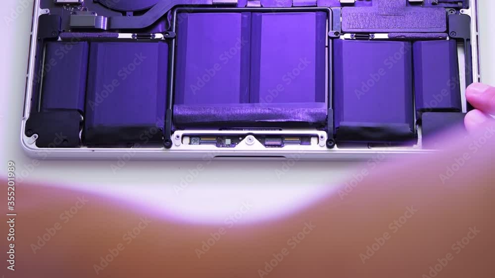 The man removes the film from the new battery after replacing it on the laptop The man removes the film from the new battery after replacing it on the laptop