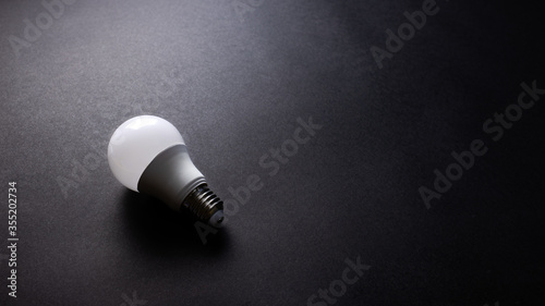 White glass light bulb on black texture background, desk from top view, copy space. 