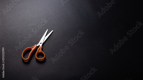 Orange steel scissors on black texture background, office desk table from top view, copy space. get over or decision concept