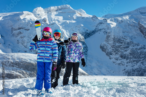Girl with ski sport equipment on shoulder stand in a group of friends over mountain peak on background