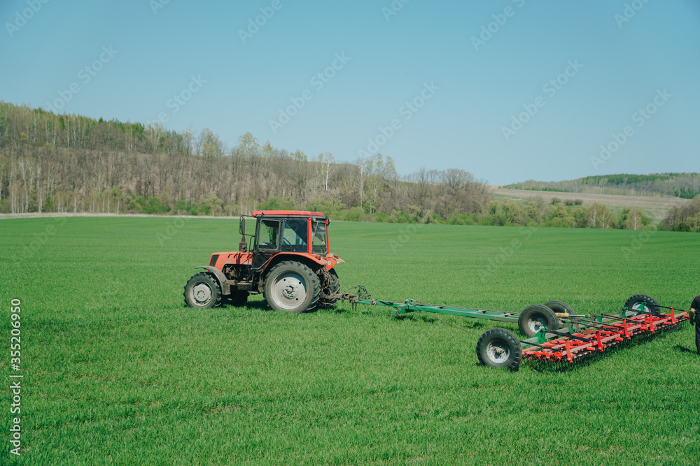 The tractor is working on a green spring field. Agriculture with cereal crops The tractor is working on a green spring field. Agriculture with cereal crops