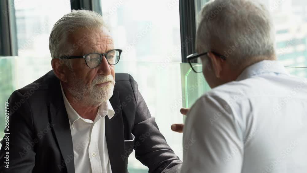 two senior businessman discussing  in modern office by window on cityscape. old man ceo consulting with client in meeting at cafe. mature manager talking with partner Listen attentively in restaurant.