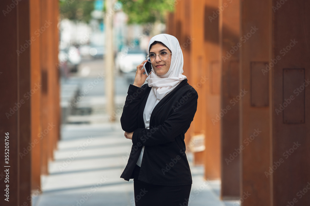 Talking on phone. Beautiful muslim successful businesswoman portrait, confident happy CEO, leader, boss or manager. Using devices, gadgets, working on go, looks busy. Charming. Inclusive, diversity.