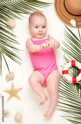 Cute baby girl with beach accessories on light background. Holidays at sea with baby, summer concept