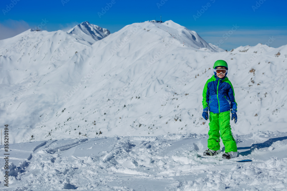 Portrait of a boy stand on snowboard over mountain in bright blue and green sport outfit mask, helmet Portrait of a boy stand on snowboard over mountain in bright blue and green sport outfit mask, helmet