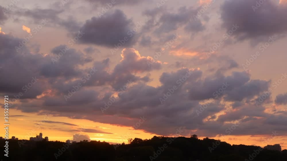 Time lapse of sunset with clouds and high rise building silhouettes on horizon 