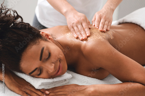 Therapist making body scrub massage for black lady photo