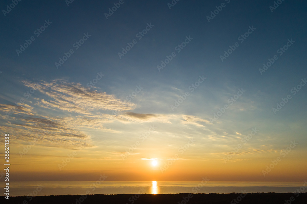 Sundown aerial view of evening sky with light clouds and sun descending to sea in Curonian spit near Nida, Lithuania