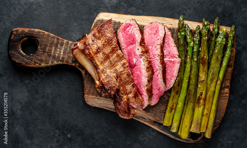 Grilled beef steak with asparagus with spices on a cutting board on a stone background