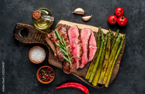 Grilled beef steak with asparagus with spices on a cutting board on a stone background