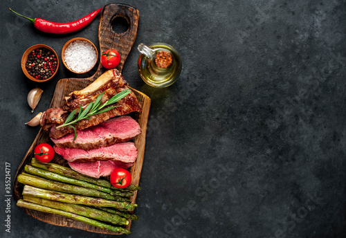 Grilled beef steak with asparagus and spices on a cutting board on a stone background with copy space for your text