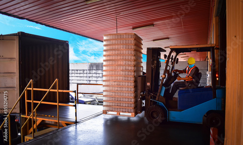 Forklift stuffing-unstuffing pallets of cargo to container on warehouse leveler dock. photo
