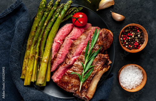  Grilled beef steak with asparagus and spices on a black plate on a stone background