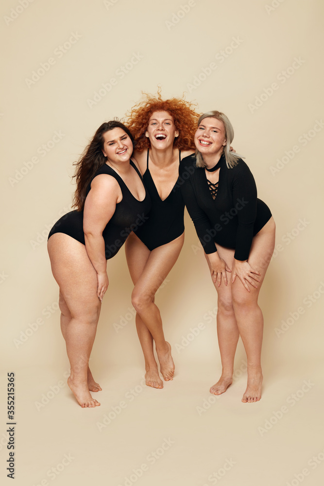 Different Body Types. Group Of Diversity Models Full-length Portrait. Cheerful Blonde, Brunette And Redhead In Black Bodysuits Posing On Beige Background. Female Friendship For Happy Life.
