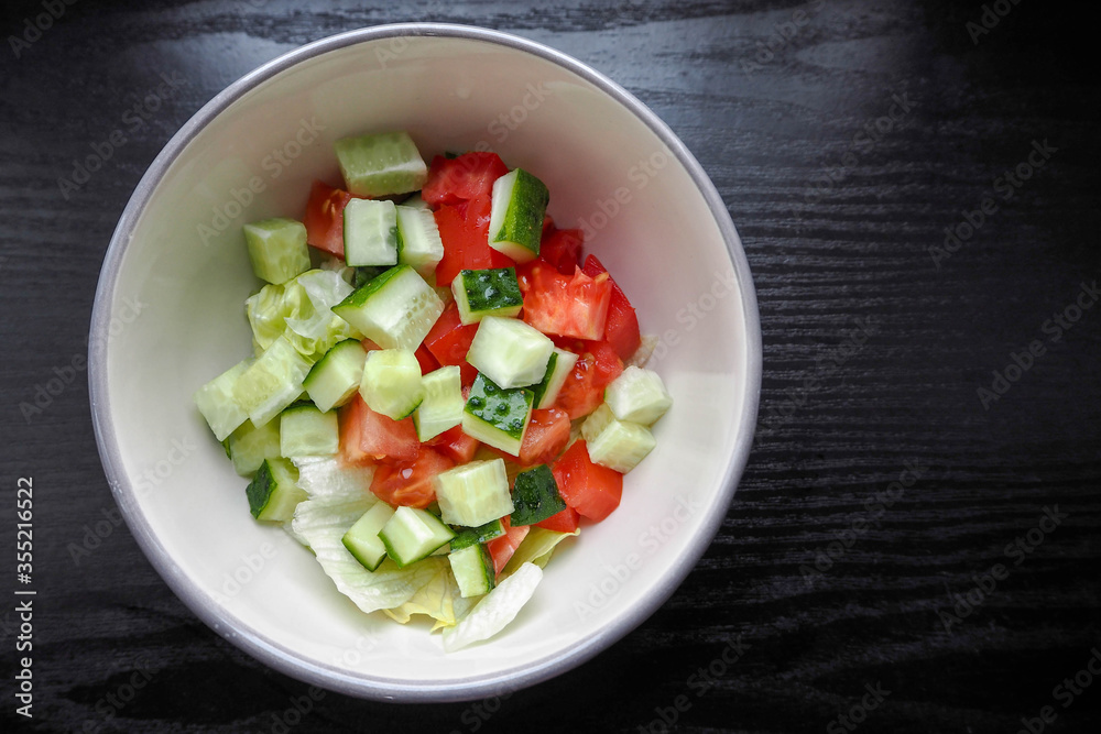 diced cucumber and tomatoes in a round beige plate before preparing a salad on a dark table background diced cucumber and tomatoes in a round beige plate before preparing a salad on a dark table background
