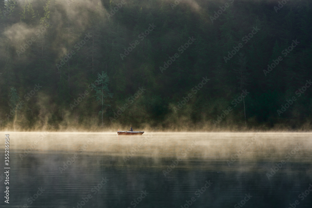 Fototapeta premium Man is rowing a boat on the foggy lake Karagol / Karagöl at sunrise. Landscape photo was taken in Savsat / Şavşat, Artvin, Karadeniz / Black Sea region of Turkey