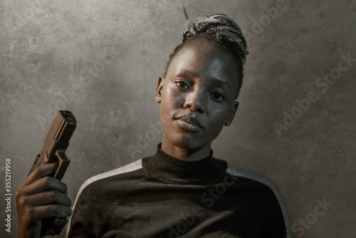 Hollywood movie style portrait of young attractive and confident black African American woman holding gun as special federal agent or mobster pointing the handgun