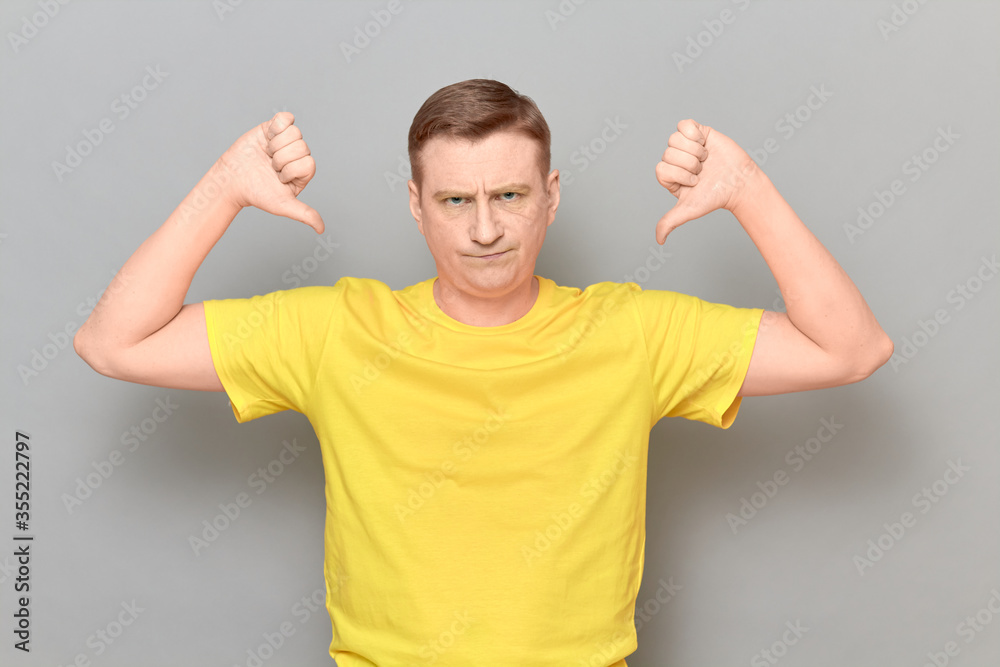 Portrait of disgruntled mature man giving thumbs down signs of dislike Portrait of disgruntled mature man giving thumbs down signs of dislike