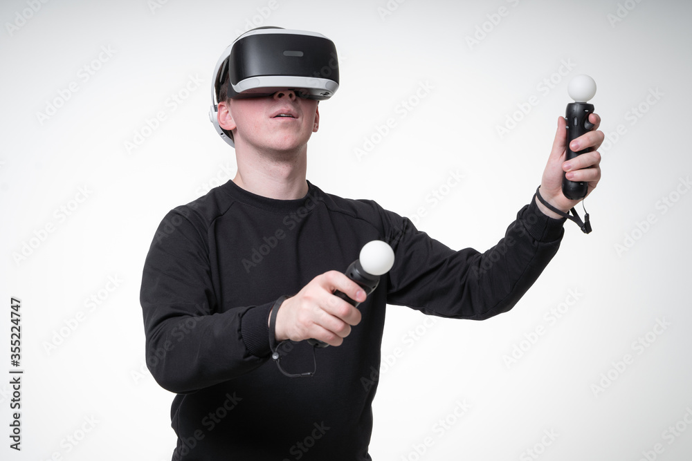 Young man is experiencing VR games with motion controllers and massive glasses, white background studio Young man is experiencing VR games with motion controllers and massive glasses, white background studio