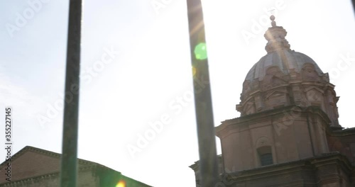 Pan shot for church building with sun flare in background against metal fences in foreground. Roman forum photo