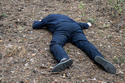 Murder in the woods. The body of a man in a blue shirt and trousers lies on the ground among the trees in the forest. Victim of an attack.