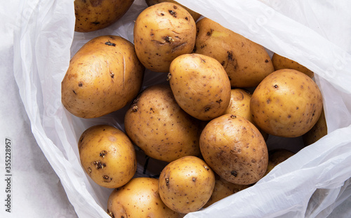 A pile of unwashed potatoes lies in a white bag