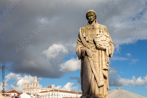 Historical statue of St. Vincent of Saragossa (Estatua de Sao Vicente de Fora) in Lisbon Portugal, sunlit against dark heavy clouds in the sky. Famous landmark and tourist attraction.