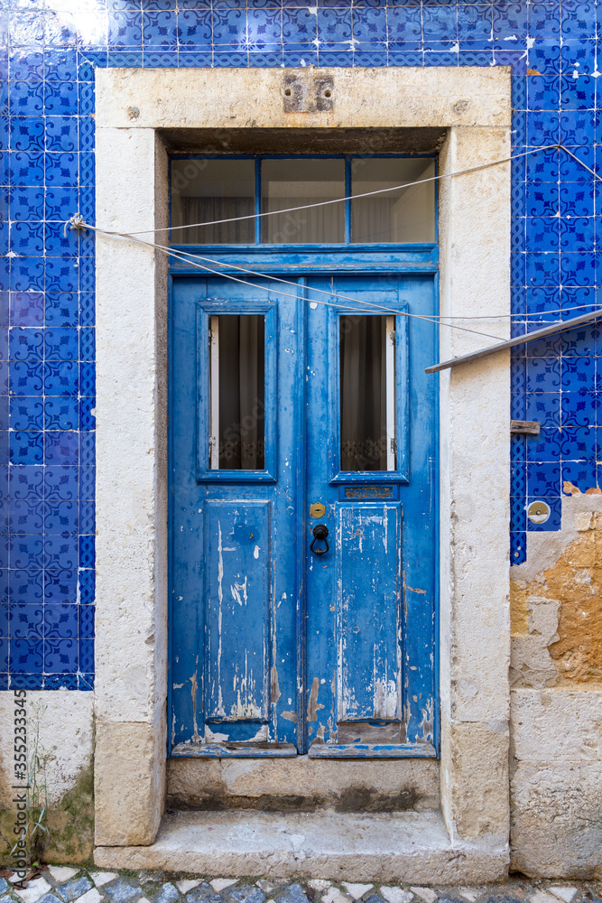 Blue aged double door made of wood on a house with azulejo facade. Empty clothes line is hanging above the entrance. In Lisbon Portugal.