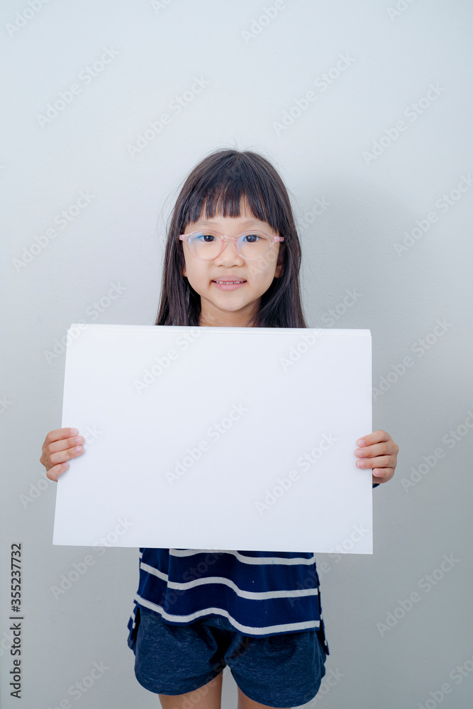 Funny little girl holds a placard plate for inscriptions. Gray background Funny little girl holds a placard plate for inscriptions. Gray background