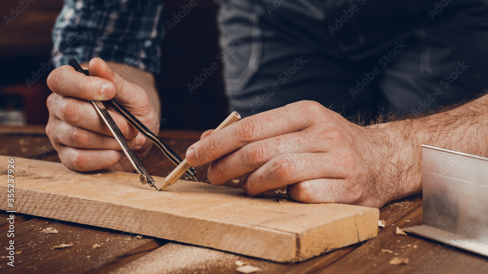 A close up of a male carpenter marks with a metal compass and pencil on a wooden bar. A close up of a male carpenter marks with a metal compass and pencil on a wooden bar.
