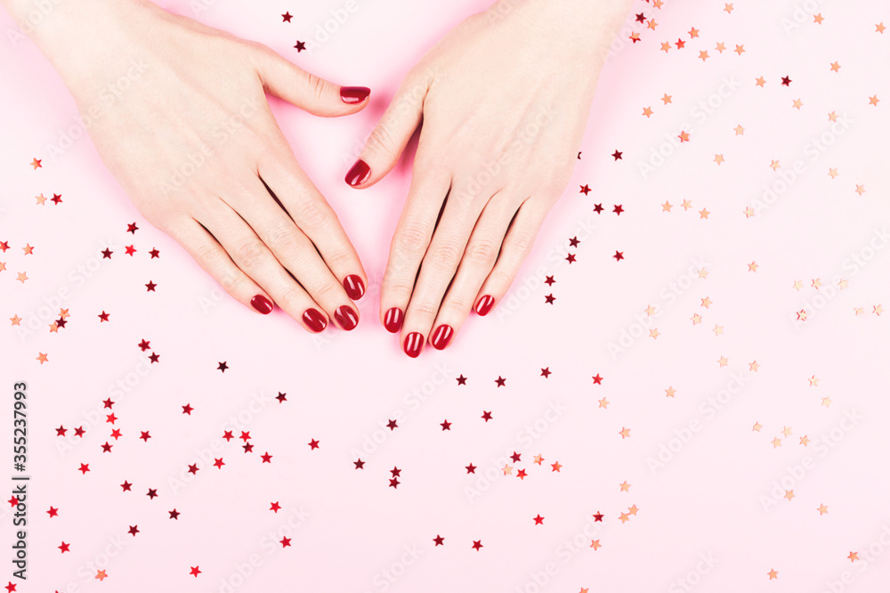 Manicure and nailcare concept. Two woman hands and falling confetti on pink background. Flat-lay, top view. Copy space.