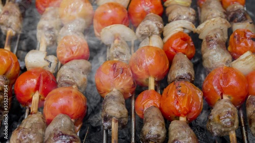 Cinemagraph of smoke emitted from cooking chicken hearts with tomato and onion on a hot BBQ grill. Close up, loop with selective focus.