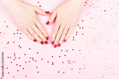 Manicure and nailcare concept. Two woman hands and falling confetti on pink background. Flat-lay, top view. Copy space.