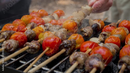 Cinemagraph of smoke emitted from cooking chicken hearts with tomato and onion on a hot BBQ grill. Close up, loop with selective focus.