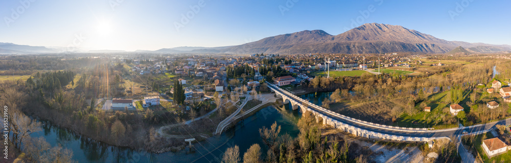 Danilovgrad Montenegro: bridge on Zeta river and Garac hill. Morning sun is low on the horizon and the sky is clear and blue. Aerial panoramic view of Bjelopavlici on the way to Ostrog monastery.