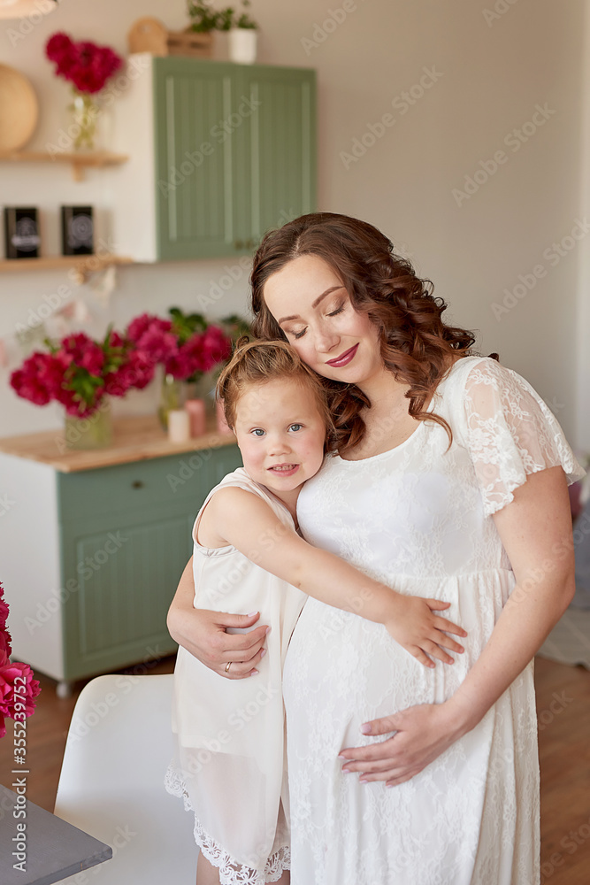 Mother's Day Greeting Card. Happy family, pregnant woman with little daughter in kitchen with peonies flowers. Relationship between parents and children. Motherhood, pregnancy, happiness concept. Mother's Day Greeting Card. Happy family, pregnant woman with little daughter in kitchen with peonies flowers. Relationship between parents and children. Motherhood, pregnancy, happiness concept.