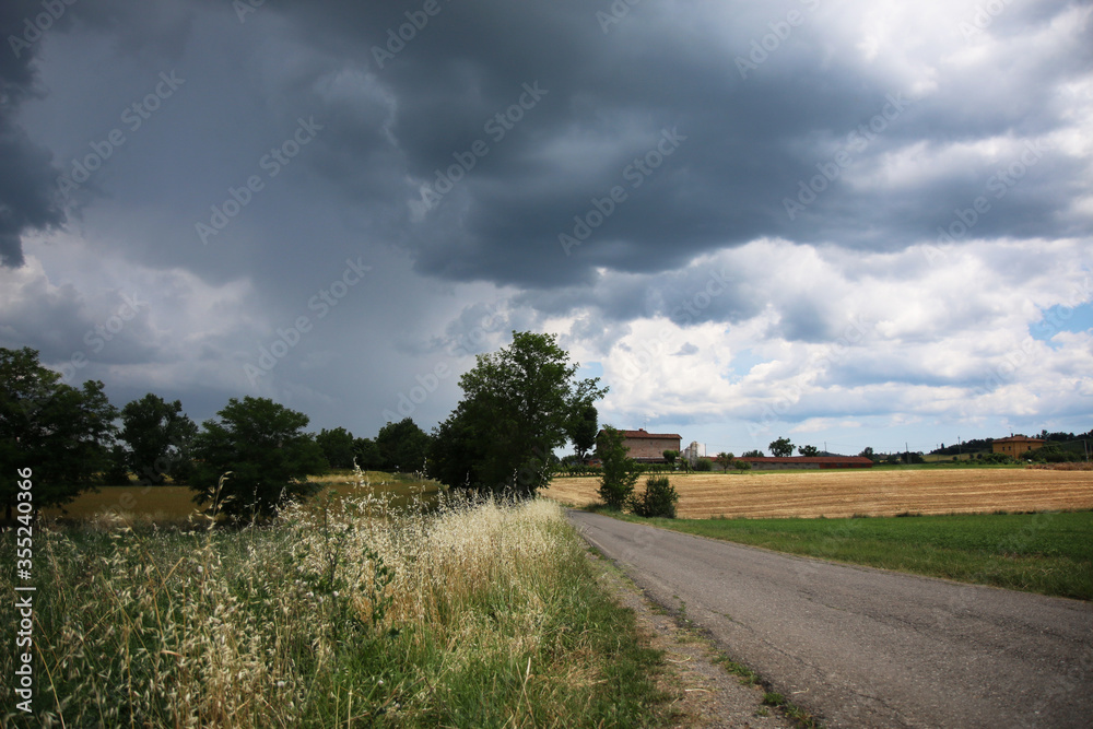 Fototapeta premium Si prepara un temporale estivo; cielo carico di nuvole e pioggia sulla campagna circostante