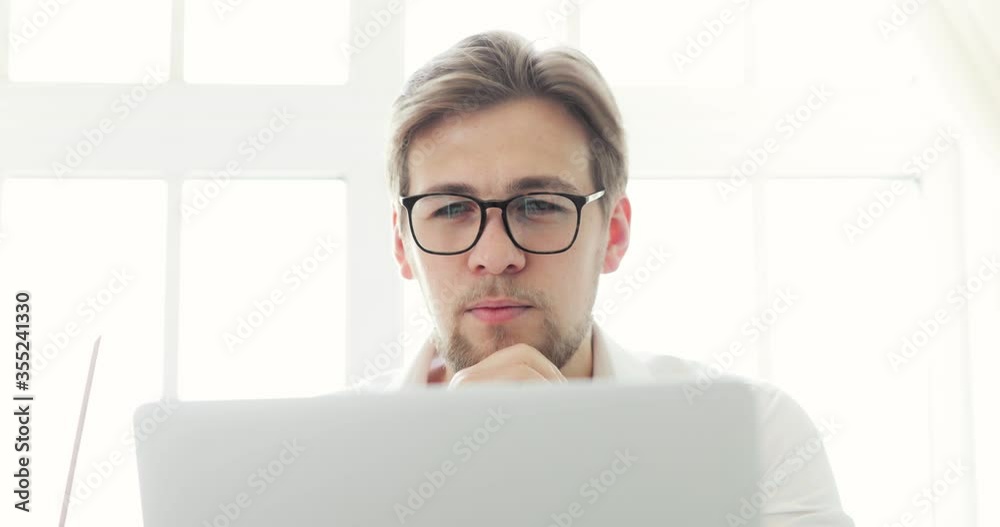 Serious man office worker working learning document on laptop at table in modern office. Portrait of businessman in glasses and white shirt at work on computer. Office work and business concept. Serious man office worker working learning document on laptop at table in modern office. Portrait of businessman in glasses and white shirt at work on computer. Office work and business concept.