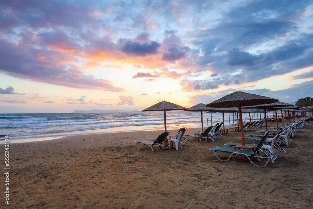 Empty beach with umbrellas and deck chairs closed. Unbelievable sunrise. 2020 summer quarantine travel. Beautiful summertime view seascape. Relax places island Crete, Greece. Empty beach with umbrellas and deck chairs closed. Unbelievable sunrise. 2020 summer quarantine travel. Beautiful summertime view seascape. Relax places island Crete, Greece.
