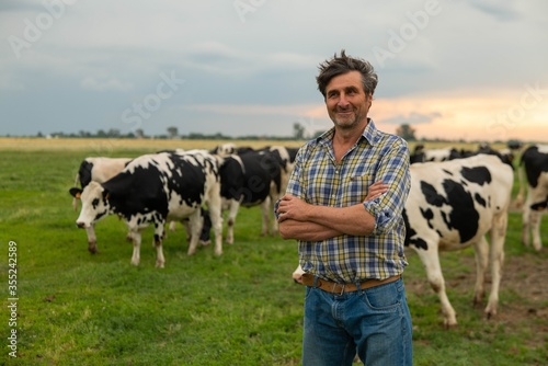 Print op canvas A mature male farmer is smiling in camera proud with his work on a countryside farm with ecologically grown cows used for biological milk products industry