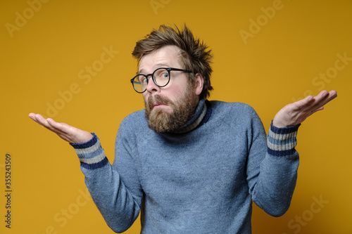 Strange man with an innocent and embarrassed expression on his face shrugs and spreads arms to the sides, on a yellow background. photo
