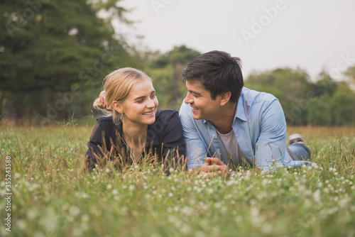 Smiling couple in love relaxing on green grass outdoor in park