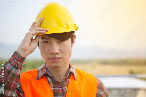 Front view of a young Asian engineer wearing reflective Orange clothing looks serious and happy. He standing on the construction project.And copy space.