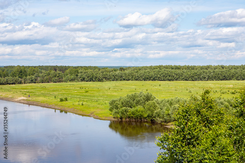 Fototapeta Naklejka Na Ścianę i Meble -  A small river flows around the forest, with the reflection of the trees in it against the blue sky. Nature of the Siberian expanses.