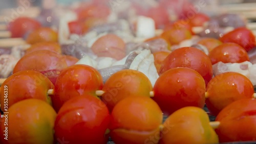 Cinemagraph of smoke emitted from cooking chicken hearts with tomato and onion on a hot BBQ grill. Close up, loop with selective focus.