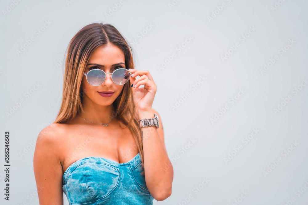 Lifestyle session, a young caucasian brunette in a blue denim dress and sunglasses on a plain gray background, with room for copy and paste Lifestyle session, a young caucasian brunette in a blue denim dress and sunglasses on a plain gray background, with room for copy and paste