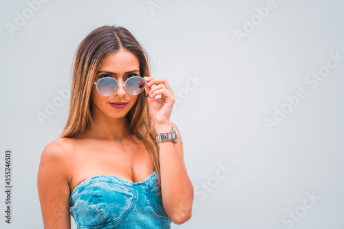 Lifestyle session, a young caucasian brunette in a blue denim dress and sunglasses on a plain gray background, with room for copy and paste