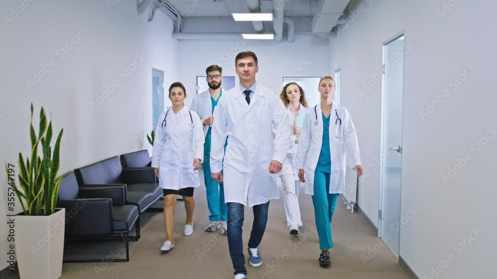 Good looking multiethnic group of doctors and nurses in a modern hospital corridor walking all together in front of the camera Good looking multiethnic group of doctors and nurses in a modern hospital corridor walking all together in front of the camera