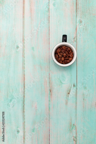 textured light blue wooden background with a small Cup with a handle with coffee roasted beans inside. brown coffee beans in a small Cup white inside and black outside on an empty wooden background