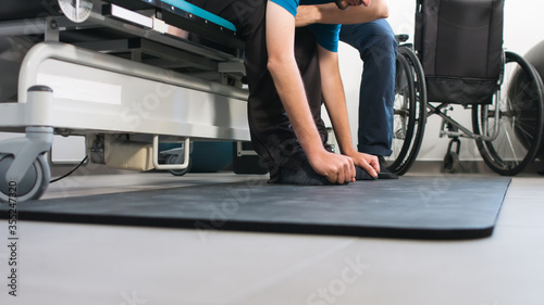 Physiotherapist exercising with disabled person using wheelchair on a therapy table.